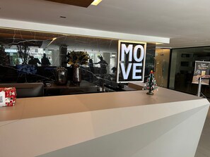 Ein Empfangsschalter mit einem 'MOVE'-Schild, eine kleine Weihnachtstanne und ein 'Cafe da Manhã'-Poster.