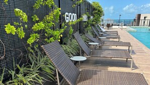 Et område ved poolen med liggestole og borde, et skilt med teksten 'GOOD VIBES' samt udsigt over poolen.