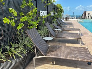 Ein Poolbereich mit Liegestühlen und Tischen, ein Schild mit der Aufschrift 'GOOD VIBES' und Blick auf den Pool.