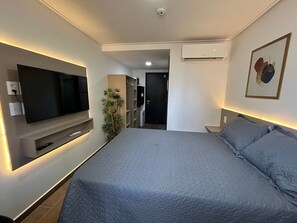 Ein modernes Hotelzimmer mit einem großen Bett, einem flachbildfernseher an der Wand, einer Zimmerpflanze und einer Klimaanlage.
