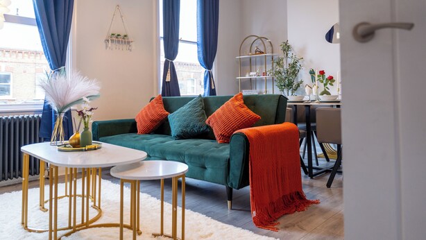 Un salon moderne avec un canapé vert, des tables rondes blanches et un tapis à poils longs blanc.