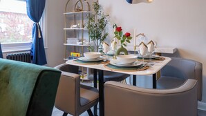 Un coin repas avec une table dressée pour quatre personnes, des chaises, un vase décoratif avec des fleurs et une étagère contenant de la verrerie.