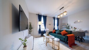 Un salon moderne avec un canapé vert, un tapis blanc et un téléviseur à écran plat fixé au mur.