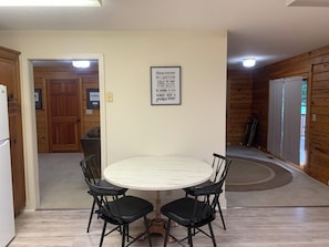 Un'area pranzo con un tavolo rotondo e quattro sedie, una porta in legno sullo sfondo e una citazione motivazionale sul muro.