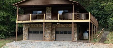 A two-story log cabin with a stone foundation, a balcony, and a garage.