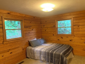 Una camera in legno con due finestre, un letto con lenzuola a righe e una lampada a soffitto.