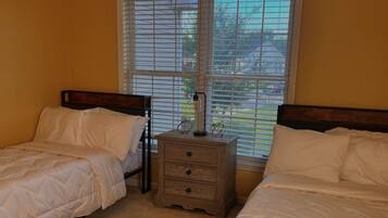A bedroom with two single beds, a nightstand with a lamp, and a window with blinds.