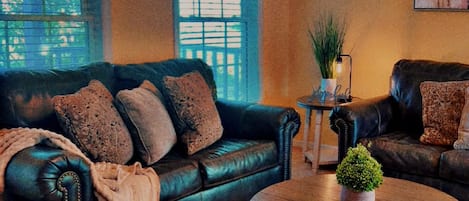 A living room with two dark leather sofas, a round wooden coffee table, and a small potted plant.