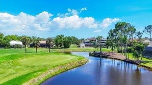 Um campo de golfe com lago, rodeado por árvores e edifícios.