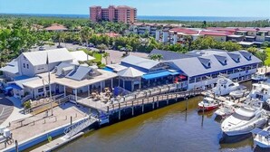 Uma marina com barcos atracados, um restaurante à beira-mar e um hotel ao fundo.