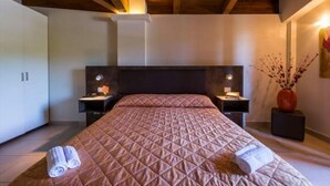 A bedroom with a large bed, wooden ceiling beams, bedside tables with lamps, and a vase with branches on the nightstand. - Hotel Centova (Perugia)