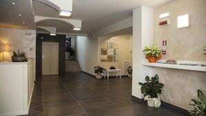A modern hotel lobby with a reception desk, a staircase, and potted plants. - Hotel Centova (Perugia)