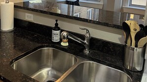 A modern kitchen with two stainless steel sinks, a black granite countertop, hanging pendant lights, and a large abstract painting on the wall. - The Lofty Loft - True City Living in Downtown Denver (Denver)