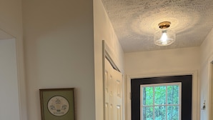 Un couloir avec une porte noire, une fenêtre, un panneau d’accueil encadré et un luminaire au plafond.