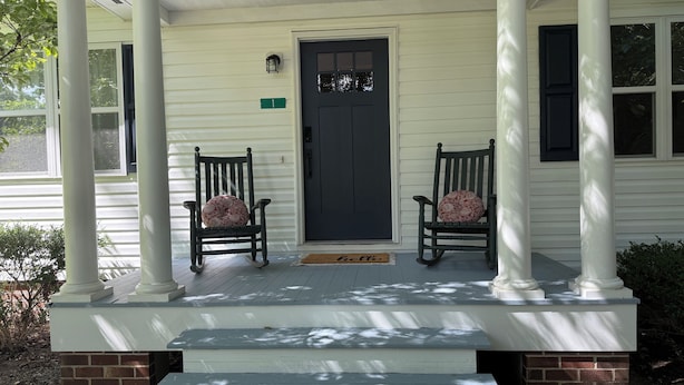 Une véranda avec deux fauteuils à bascule, une porte noire et une boîte aux lettres.