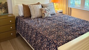 Une chambre à coucher avec un lit, une table de chevet, une lampe, une fenêtre avec des rideaux et un tableau au mur.