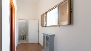 Un couloir étroit doté d’un sol carrelé, d’une armoire et d’une porte donnant sur une salle de bain avec douche et toilettes.