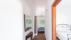 Un couloir étroit avec un lit à droite, un canapé au milieu et un miroir à gauche.