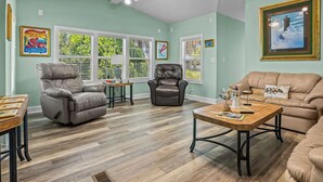 A spacious living room with a high ceiling, two leather sofas, a coffee table, and a ceiling fan.