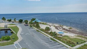 A coastal parking lot with a view of the ocean, a beach area with umbrellas, and a small dock.