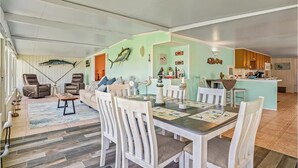 A spacious living room with a dining area, featuring a large fish mounted on the wall, a fireplace, and a kitchen in the background.