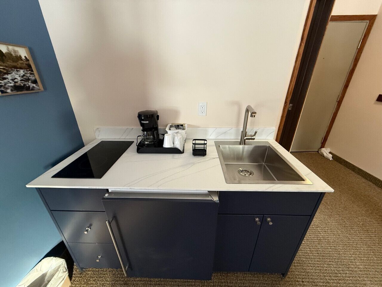 A compact kitchen with a double sink, a coffee maker, and a small cabinet.