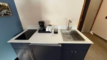 A compact kitchen with a double sink, a coffee maker, and a small cabinet.