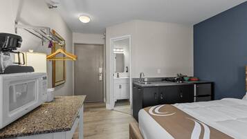 A compact hotel room with a kitchenette, a bed with a brown headboard, and a door leading to a bathroom.