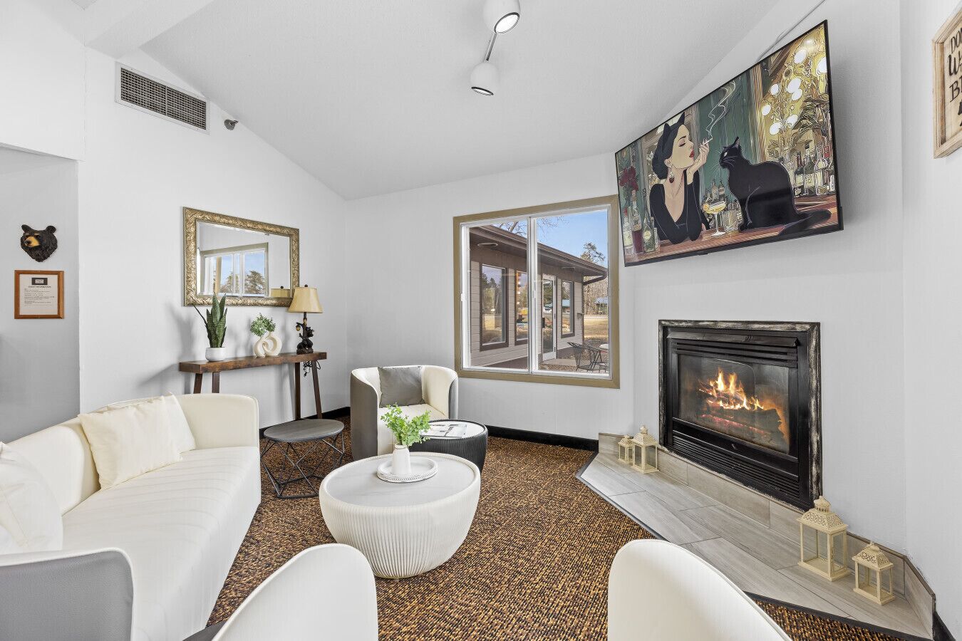 Un salon moderne avec une cheminée, des meubles blancs, une grande fenêtre et un tableau représentant un chat.