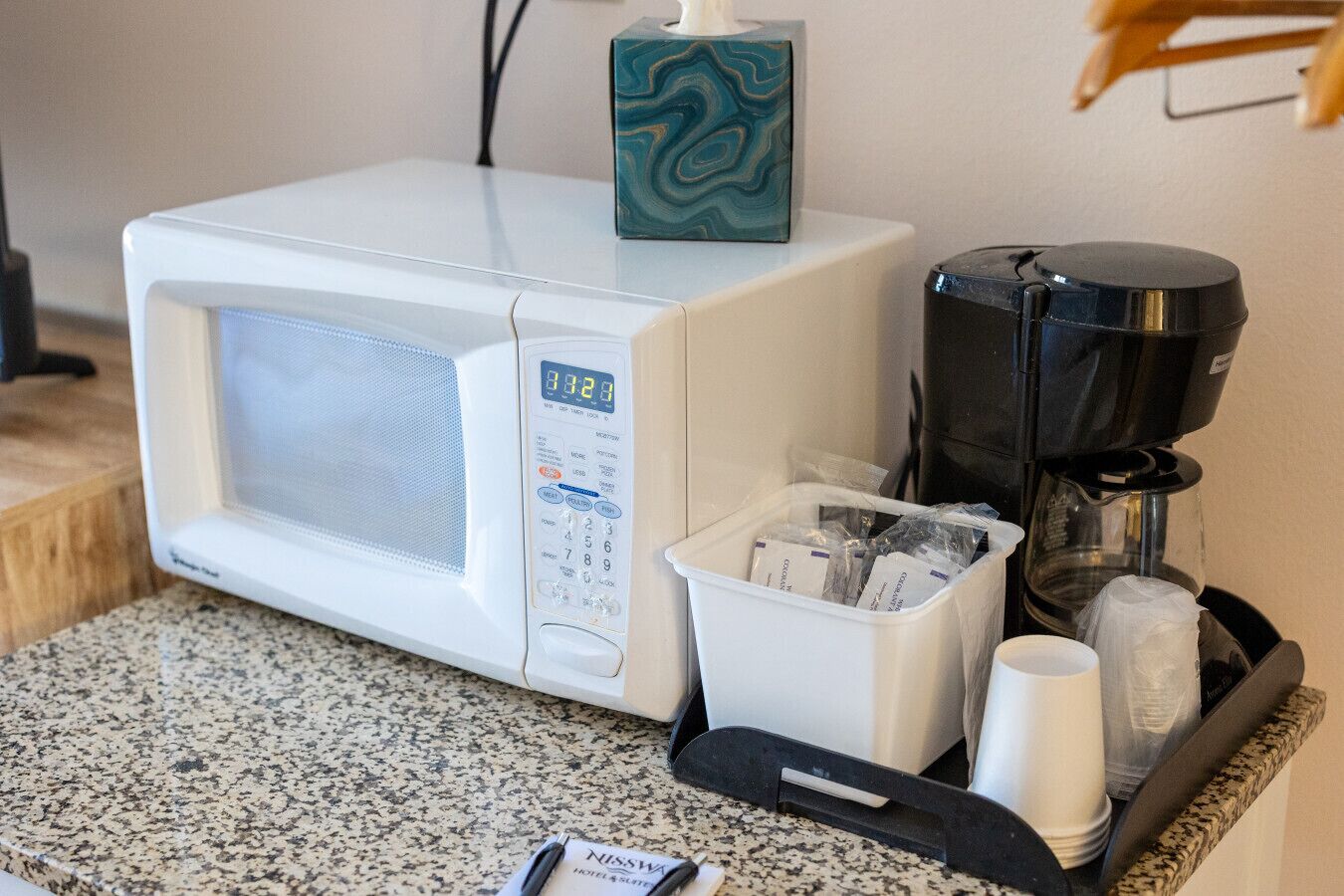 Un microondas, una cafetera y un recipiente con sobrecitos en una encimera.