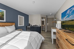 A hotel room with a large bed, a dresser, a desk, a mirror, a television, and a bathroom visible through an open door.