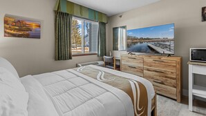 Habitación de hotel con una cama grande, un aparador de madera, una televisión y una ventana con cortinas.