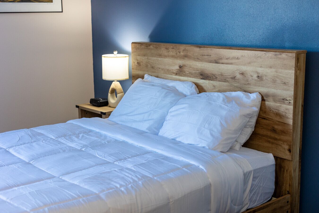 A neatly made bed with white linens, a wooden headboard, and a bedside lamp.