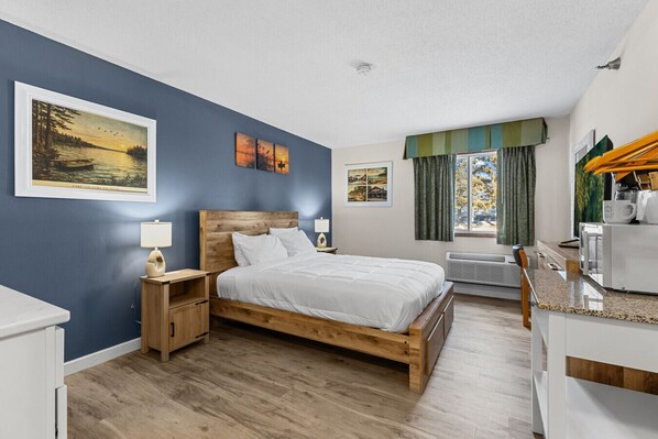 A bedroom with a wooden bed, a nightstand, a desk, and a window with curtains.