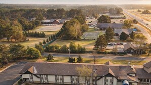 An aerial view of a small town with a prominent building with a large garage door, surrounded by trees and a road. - Nisswa Hotel & Suites – Cullen Lake Jacuzzi King (Nisswa)