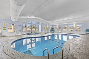 Ein Hallenbad mit großen Fenstern, einem Rettungsschwimmerstuhl und einem Schild mit den Spa-Regeln.