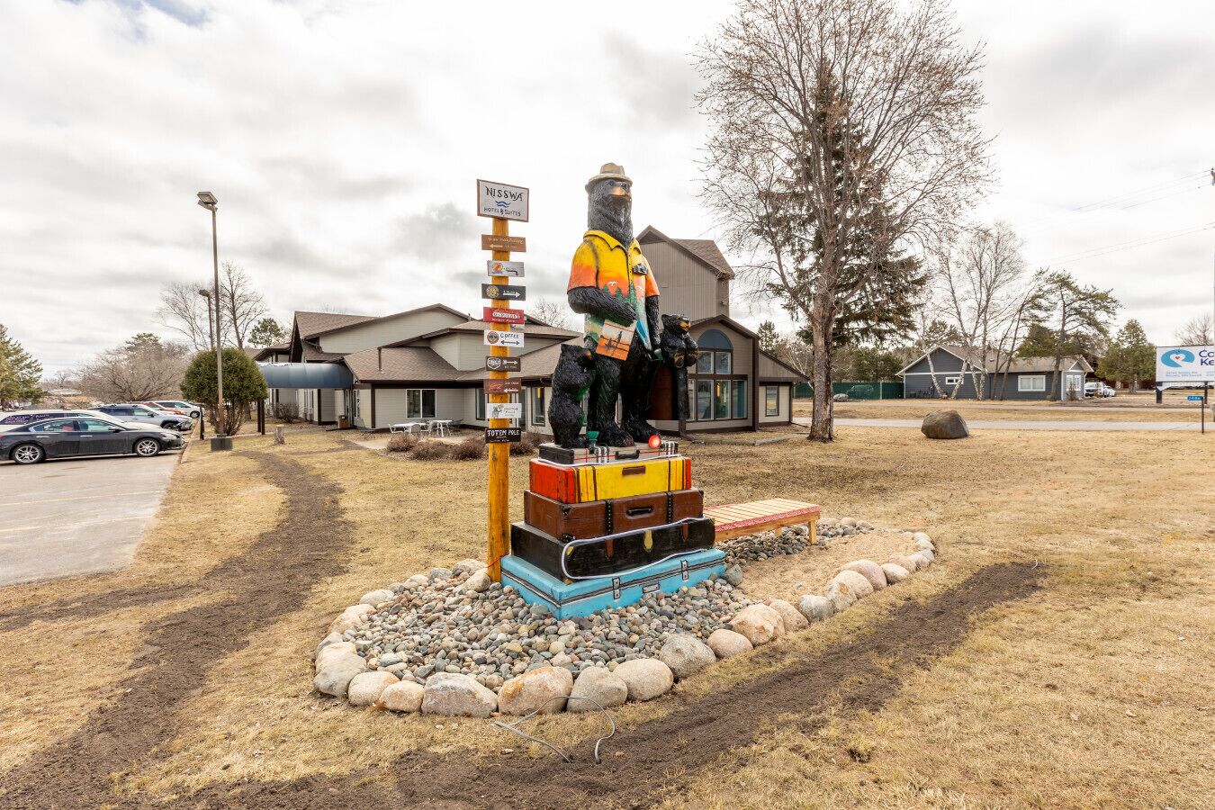 A bear statue with a signpost, surrounded by rocks and a parking lot.