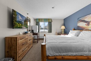 Ein Schlafzimmer mit einem Bett, einem Holzschrank, einem Schreibtisch und einem großen Fenster mit Vorhängen.