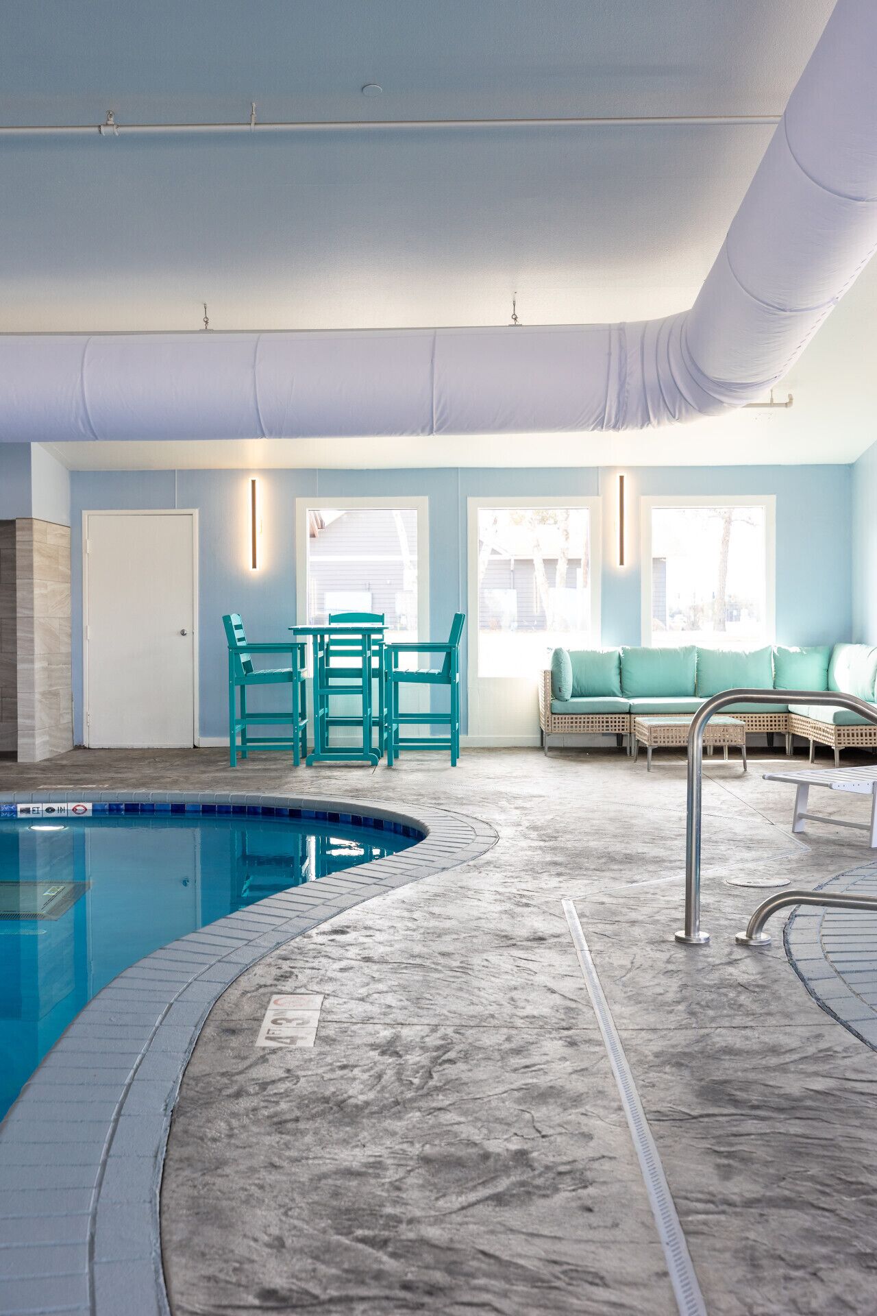 An indoor swimming pool with a tiled floor, a seating area with a sofa and chairs, and a window providing natural light.