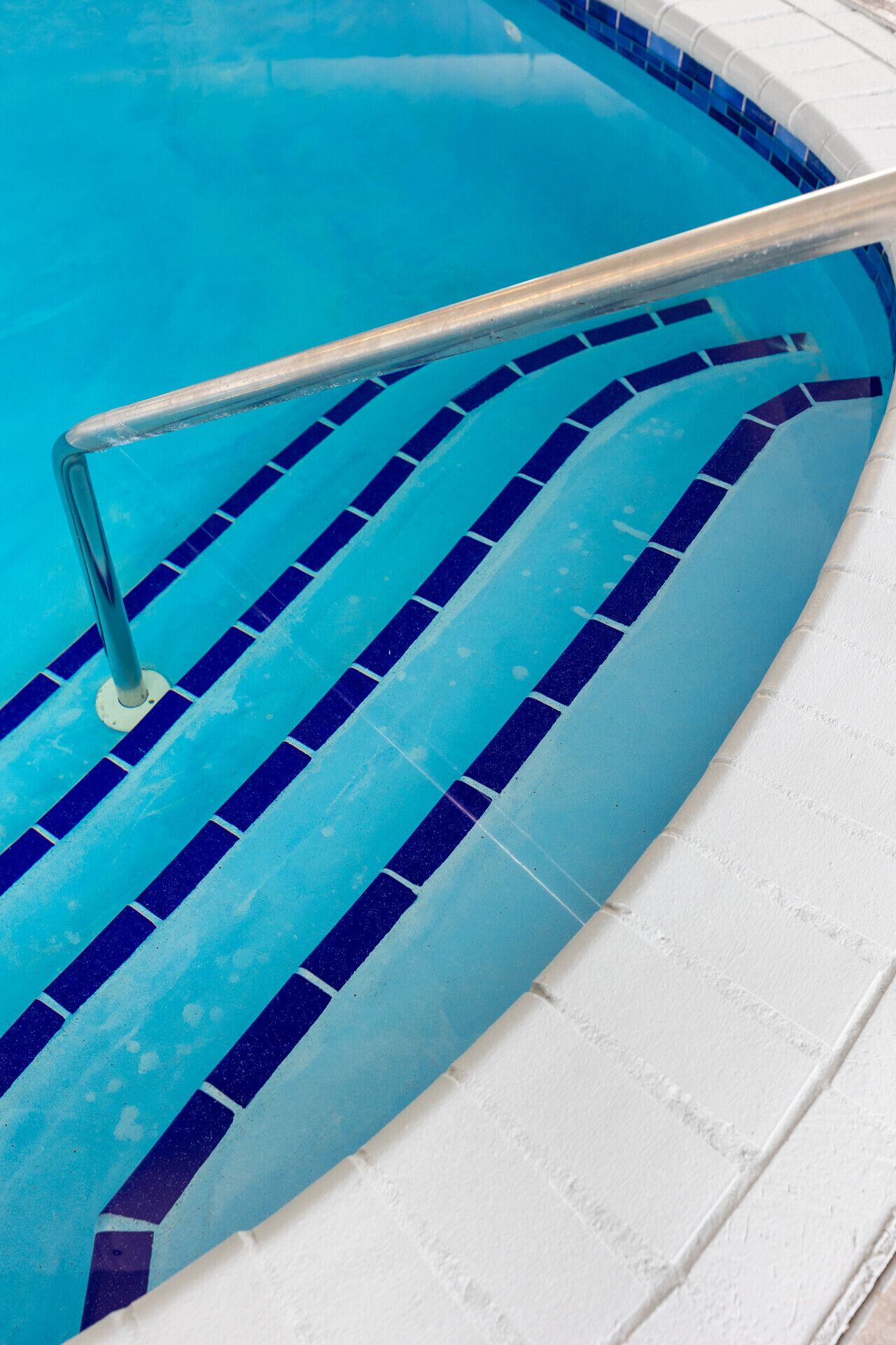Una piscina con escalones de cerámica azul y blanca y una barandilla de metal.