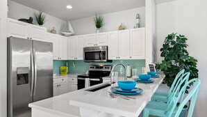 A modern kitchen with white cabinets, stainless steel appliances, and a central island with blue bowls. - Beach and Bay Bliss at Bermuda Bay Club/Poolside (Bradenton Beach)