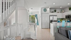 A modern kitchen with white cabinets, a stainless steel refrigerator, and a dining area with a gray sofa and turquoise chairs. - Beach and Bay Bliss at Bermuda Bay Club/Poolside (Bradenton Beach)