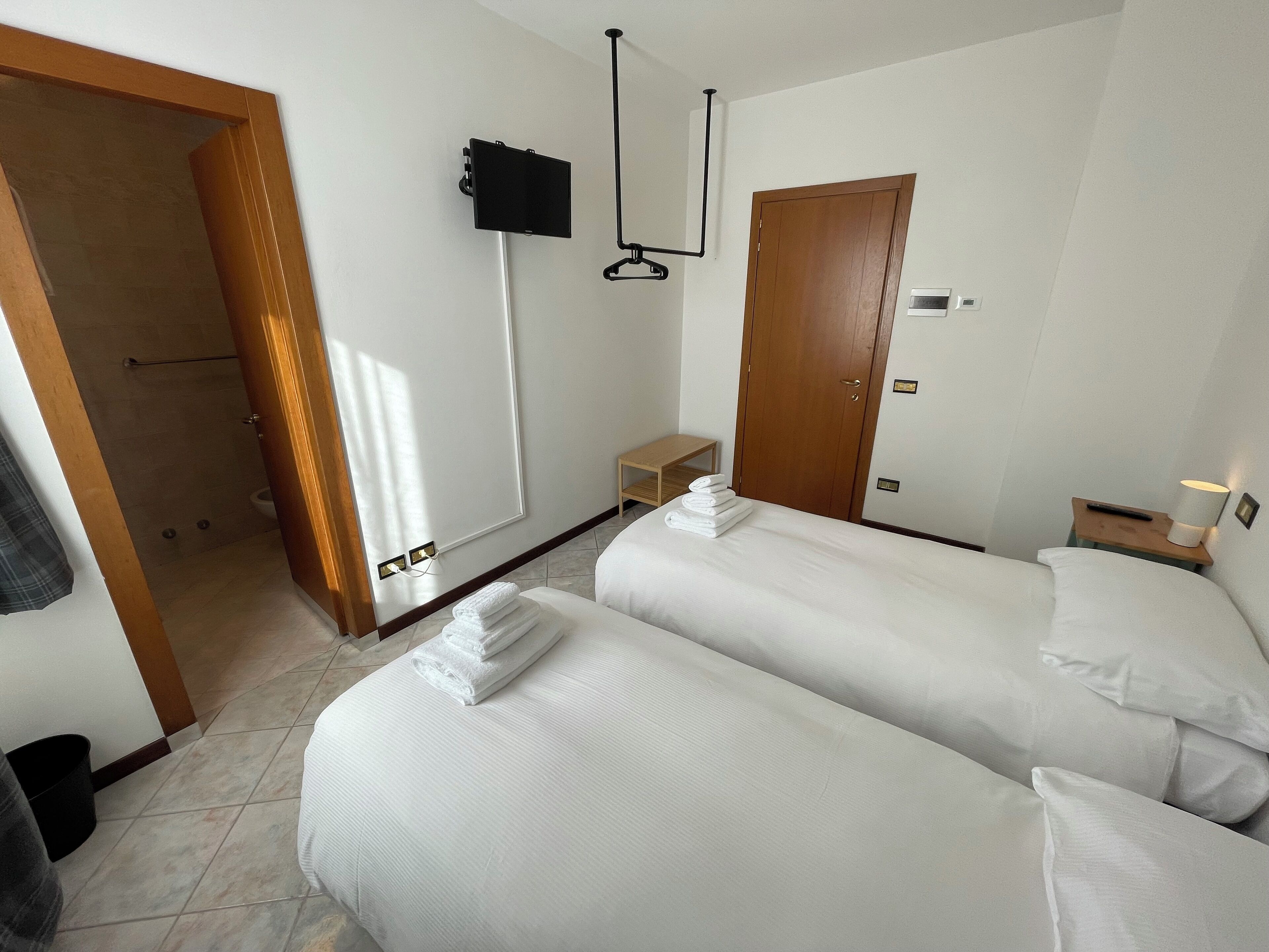 Une chambre d’hôtel avec deux lits, un téléviseur fixé au mur, une porte en bois et une petite table avec une lampe.