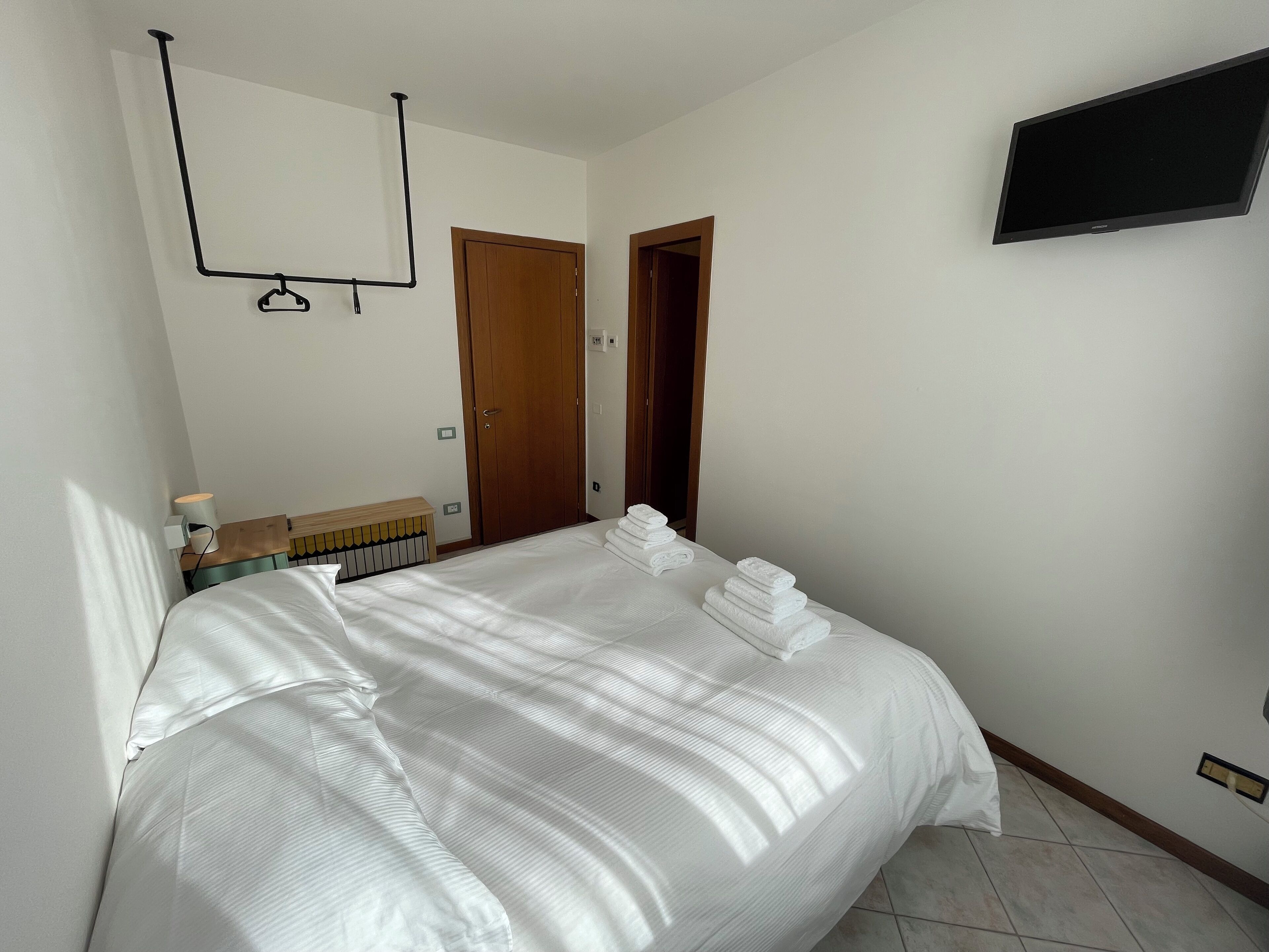 Une chambre d’hôtel avec un lit bien fait, une tête de lit en bois, un téléviseur fixé au mur et une porte donnant sur une autre pièce.