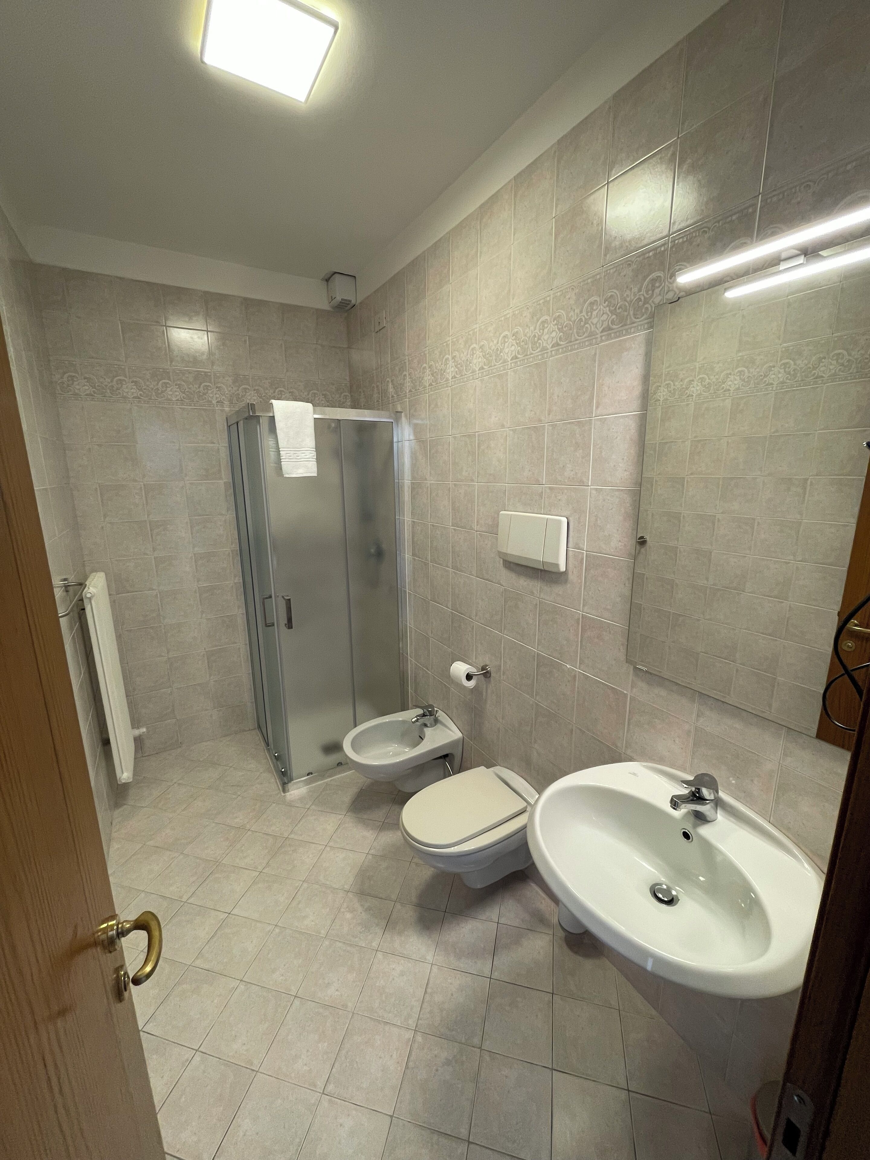 A bathroom with a toilet, bidet, and sink, tiled walls, and a shower.