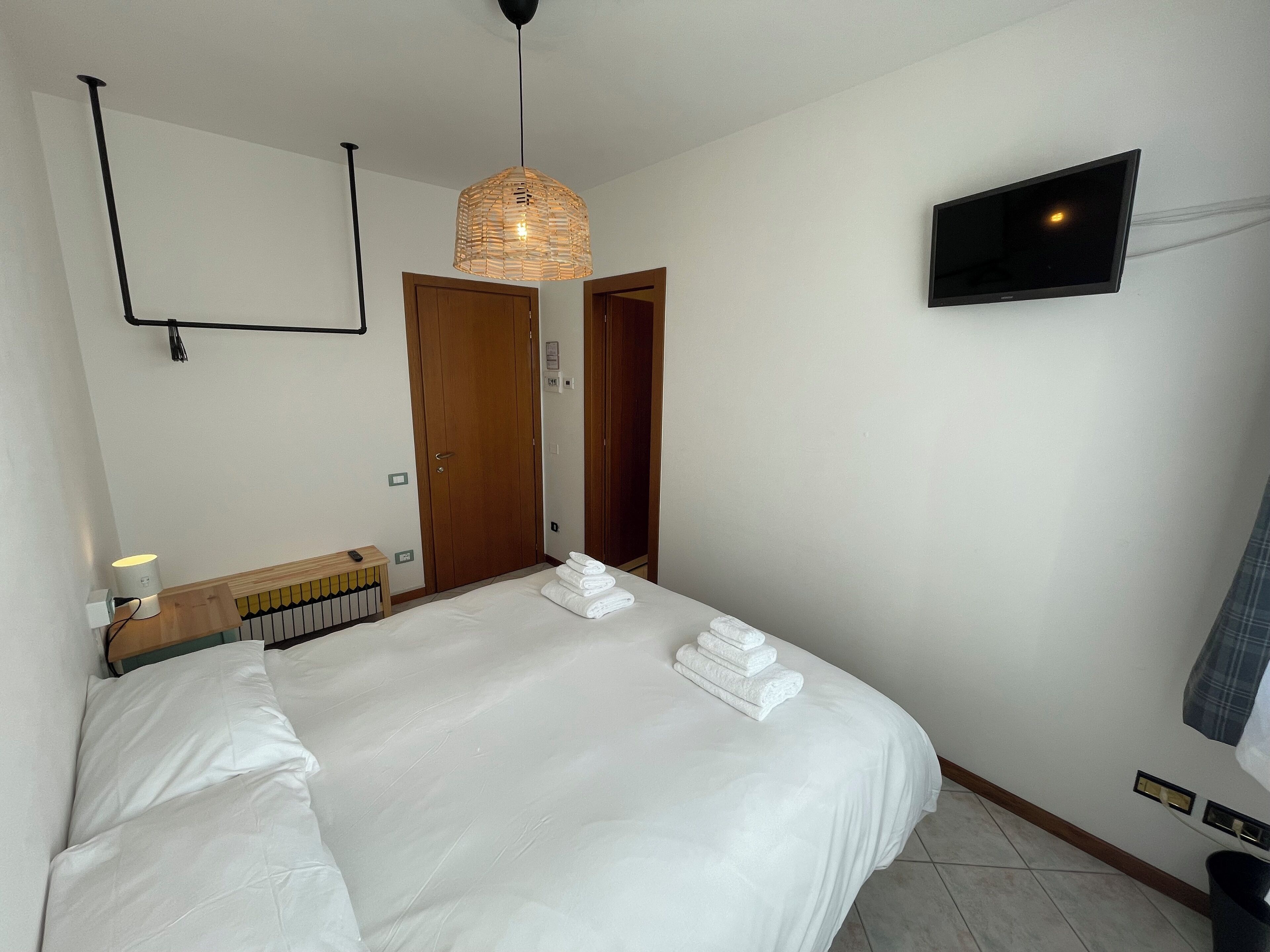 A hotel room with a large bed, a bedside table with a lamp, a television mounted on the wall, and a door leading to another room.