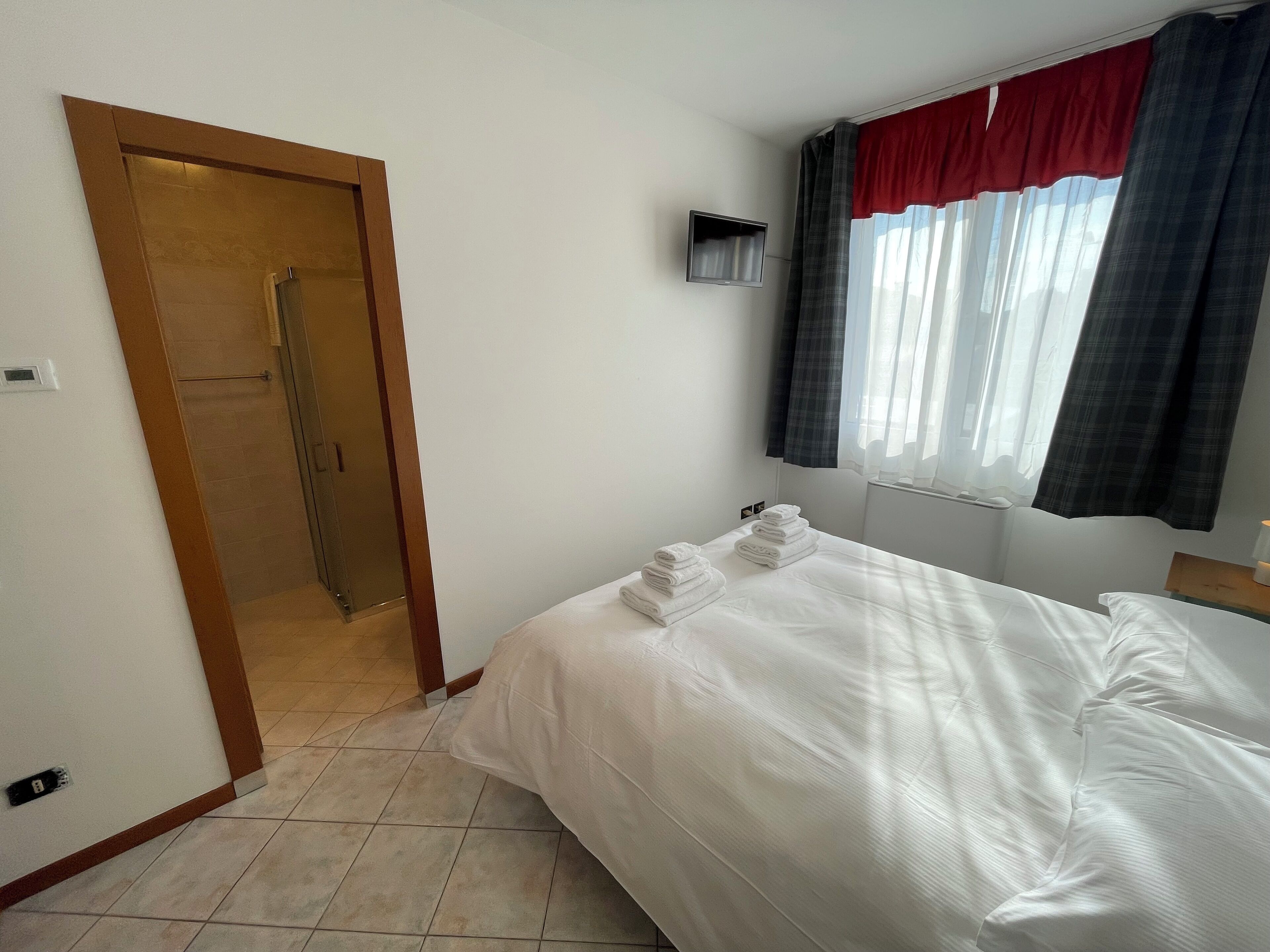 Ein Hotelzimmer mit Bett, Dusche, Fernseher und einem Fenster mit Vorhängen.