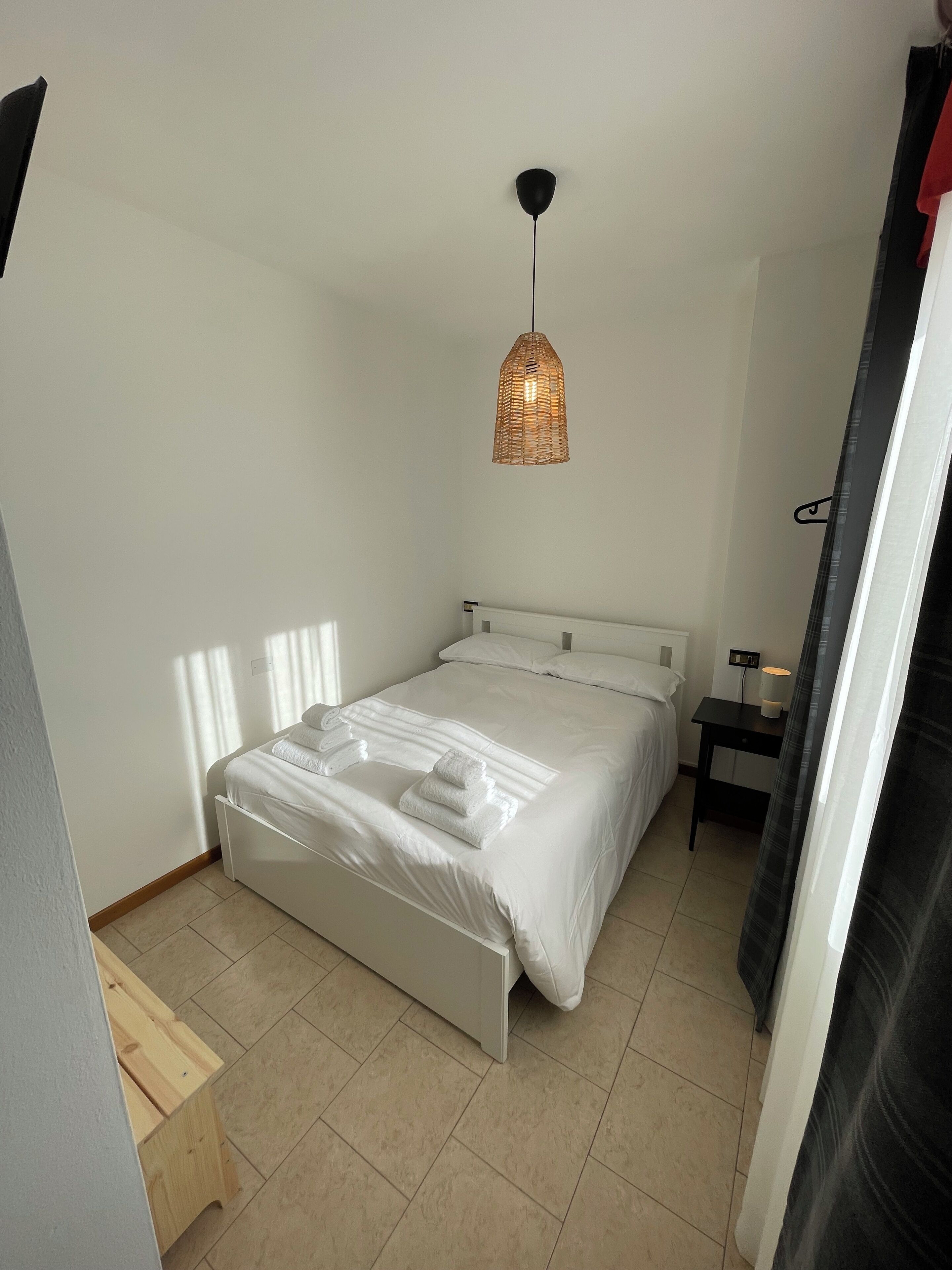 A neatly made bed with white linens and a small bedside table with a lamp.