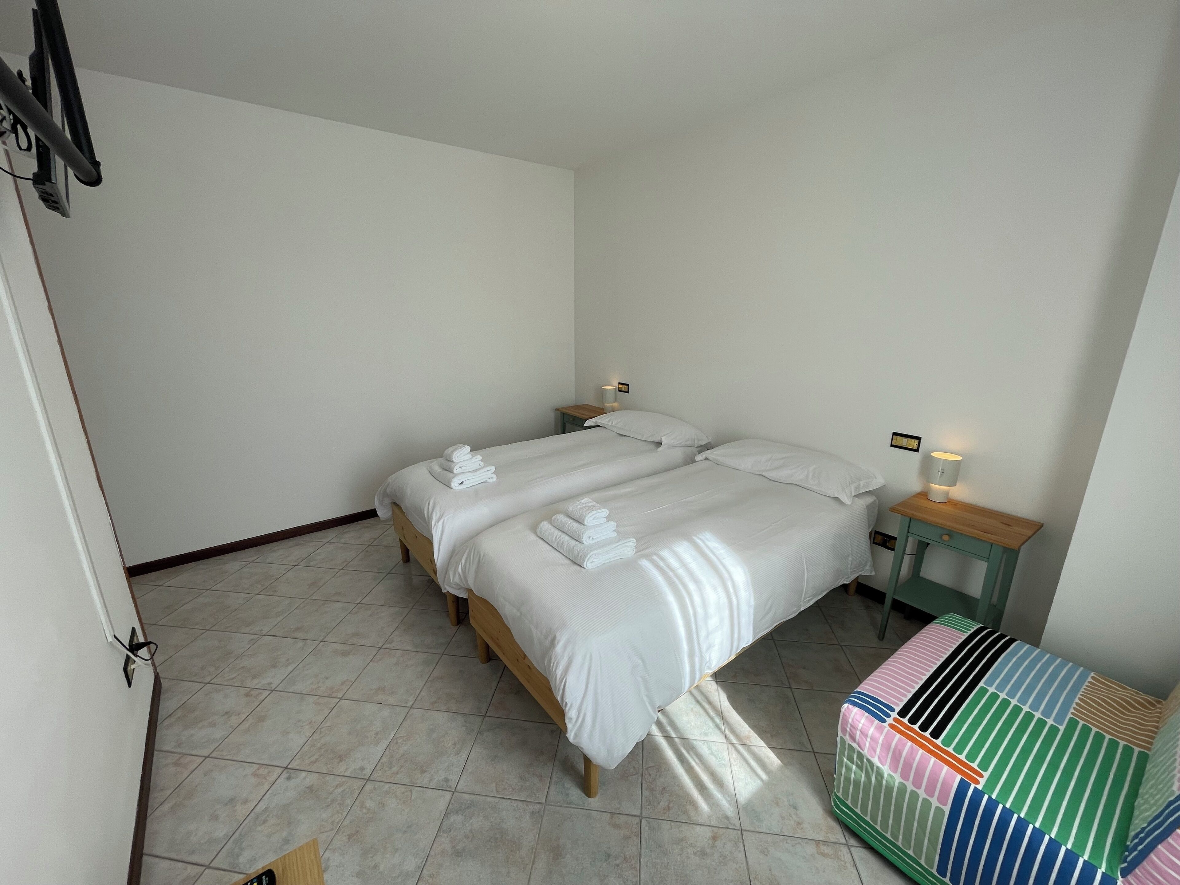 A clean, well-lit bedroom with two beds, a nightstand, and a colorful sofa.