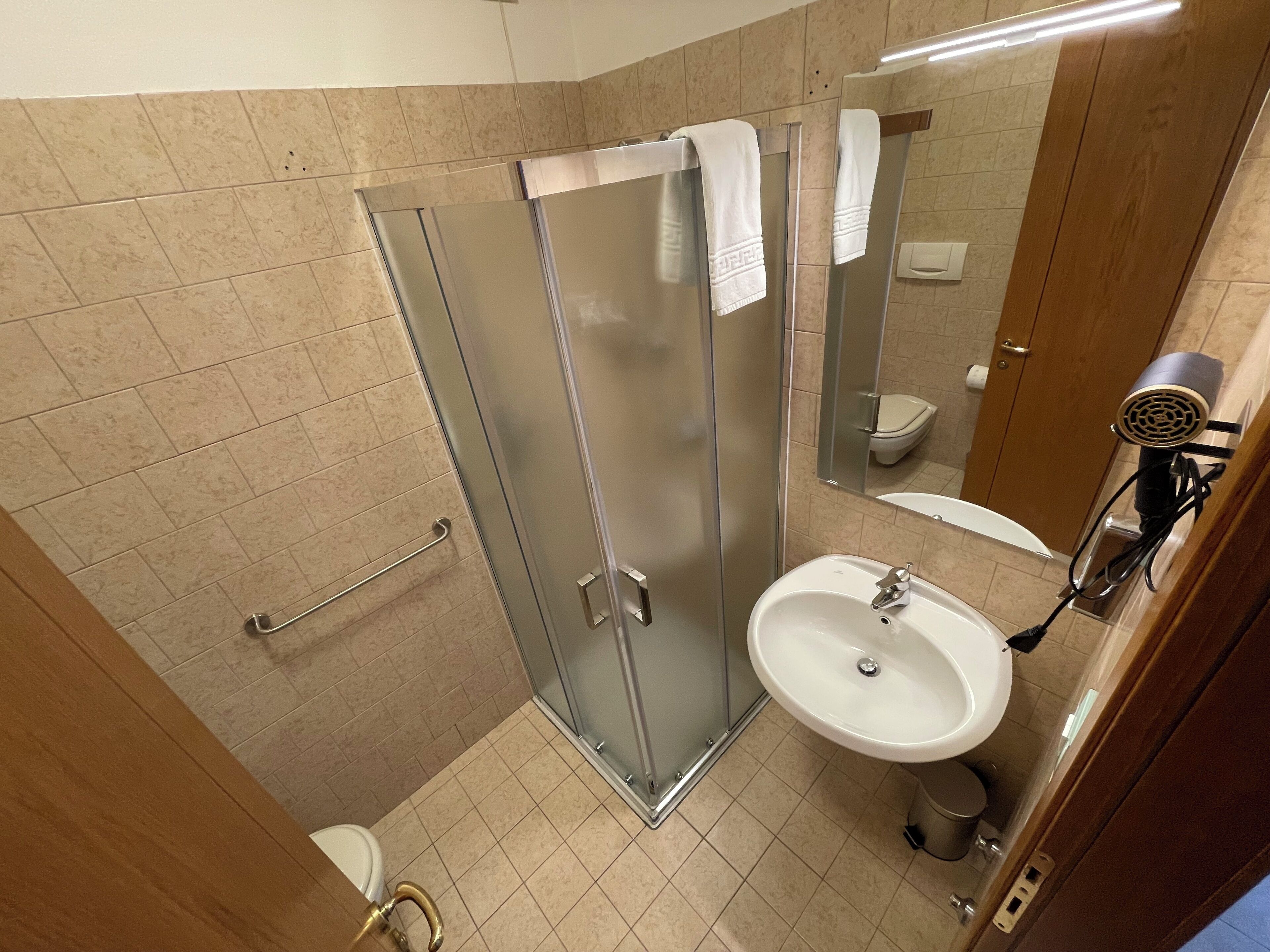 A bathroom with a glass shower enclosure, a sink, a toilet, and a hairdryer mounted on the wall.